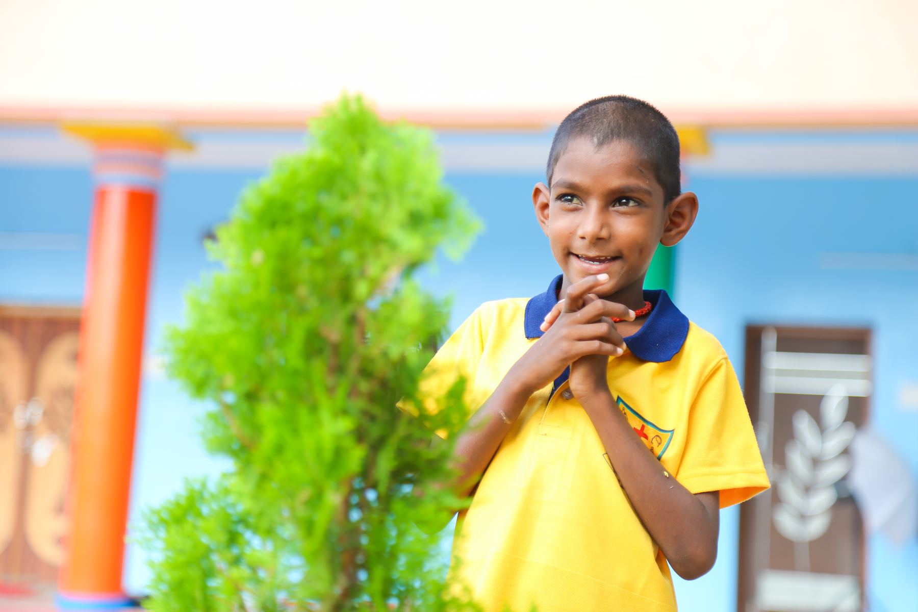 A smiling boy standing beside a plant at the home